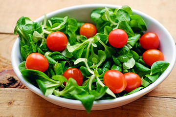 Cherry tomatoes and basil salad in a white cup on a wooden table.