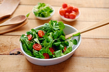 Cherry tomatoes and basil salad on a plate with a pot on a wooden table.
