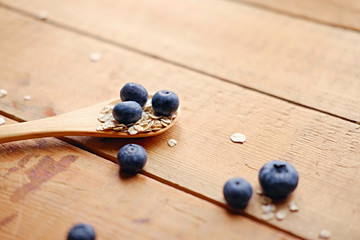 Wooden spoon with oat flakes and blueberry over wooden pattern background.