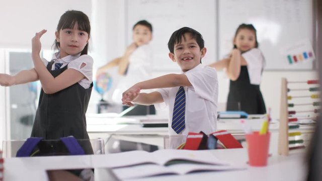  Happy group of Asian children doing physical exercises in school classroom