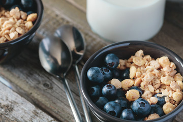 Granola with fresh blueberries in black bowl on a rustic old wooden table. 