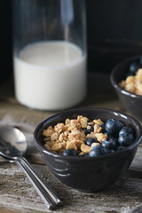 Granola with fresh blueberries in black bowl on a rustic old wooden table. 