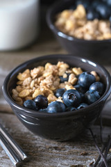 Granola with fresh blueberries in black bowl on a rustic old wooden table. 