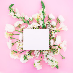 Flat lay frame with paper card, white ranunculus, snapdragon, tulip and freesia isolated on pink background. Top view