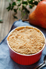 Close-up of a portion dessert pear crumble pie in a red bowl on a wooden table.