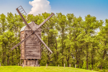 Fototapeta na wymiar Wooden windmill on a background of green trees. Summer rural landscape.