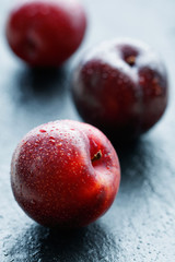 Close-up of fresh red plums on a dark table.