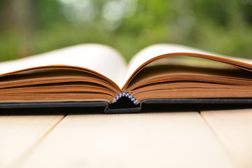 Open old book on wooden table and nature background