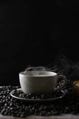 White coffee cup with coffee and coffee beans with smoke and on wooden background.