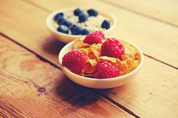 Golden corn flakes, Hercules oat and some berries in a cup on a wooden table.