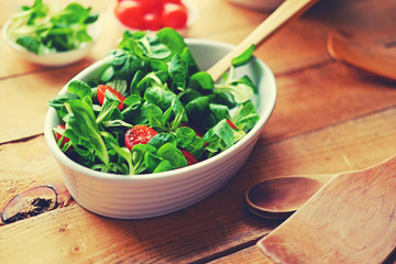 Cherry tomatoes and basil salad on a plate with a pot on a wooden table.