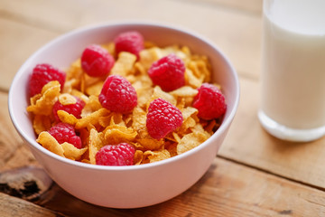 Diet corn flakes with raspberry and glass with milk on a wooden table.