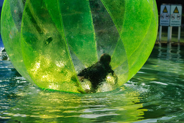 Children have fun inside plastic balloons on the water.