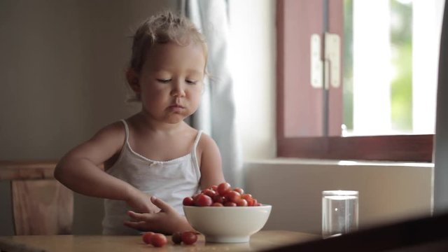 Portrait of cute baby girl eating red cherry tomato