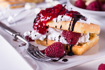 Belgian waffles with raspberries and double cream on white plate.