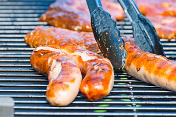 Brat sausage is served on the charcoal grill with the grill tongs