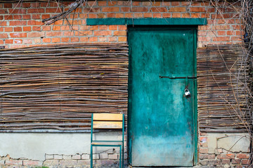 Turquoise door with wooden branches and a chair from natural wood picturesque background