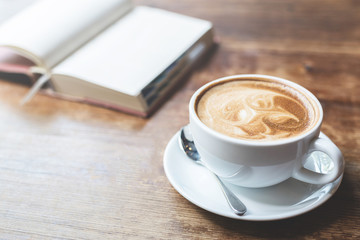 A cup of coffee with open notebook on wooden table.