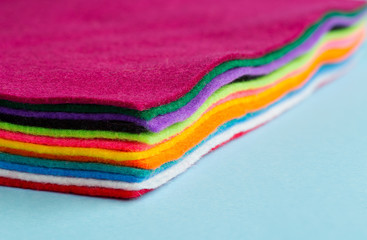 Semi-abstract of a pile of brightly coloured rainbow felt material on a plain light blue surface