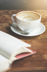 A cup of coffee with open notebook on wooden table.