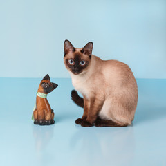 The Thai cat is sitting next to the wooden figurine of a Thai cat.