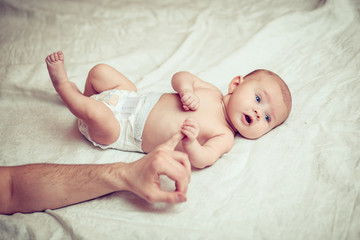 happy baby lying on white sheet and holding his legs