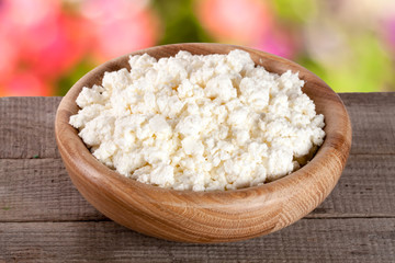 Cottage cheese in a wooden bowl on board with blurred garden background