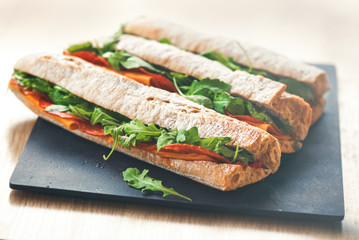 Healthy fresh crusty baguette submarine sandwich with salami, cheese and rucola. Selective focus