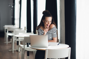 Photo of pretty woman fiddling with pen and thinking over a subject while sitting in some coffee shop with her laptop.