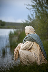 Jesus Christ crouched next to a body of water and pondering 