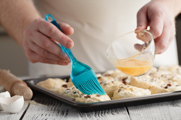 Smearing raw buns with brush in yolk, preparation process