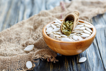 Pumpkin seeds and wooden scoop in bowl.