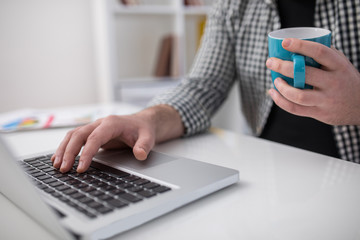 Fototapeta premium Close up of male hand holding a coffee cup in office and using laptop