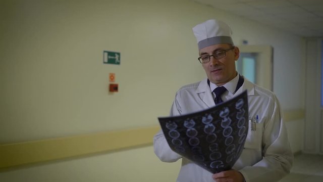 Male doctor analysing radiogram. Male doctor wearing uniform and walking in hospital hallway with radiogram in hands.