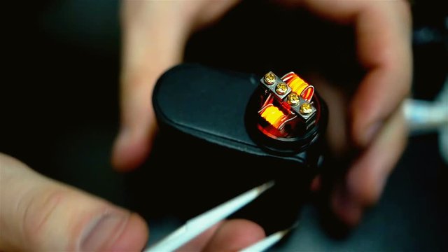 Vape after-sales service of the e-cigarette. Male hands regulate electronic cigarette coils. Glowing spiral for background. Personal vaporizer.