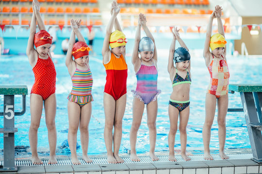 Instructor and group of children doing exercises near a swimming pool