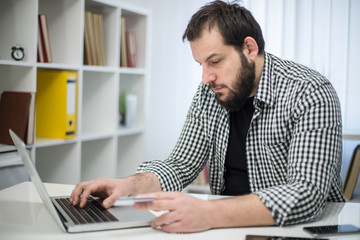 Bearded young man in office online shopping with credit card