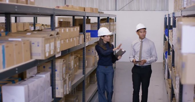  Business man & woman in discussion as they walk through industrial warehouse.