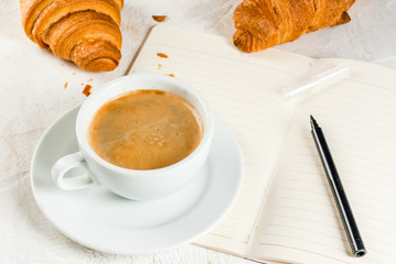 Relaxation. Job. Planning of affairs. White stone table with a notebook for notes, cases, tasks. A cup of fragrant freshly brewed coffee. Freshly baked croissants. Pencil. Copy space top view