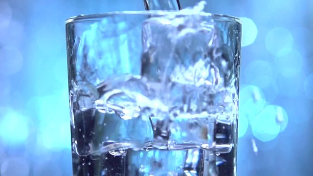 Water is pouring into a glass with ice cubes. Clear water pours ice cubes on a blue flickering background. Pure water  with Ice and bubbles in glass. Full HD  footage 1920x1080p. Slow motion 240 fps