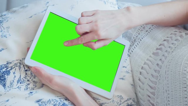 Young Woman in white dress laying on couch uses Tablet PC with pre-keyed green screen. Few types of gestures - scrolling up and down, tapping, zoom in and out. Perfect for screen compositing