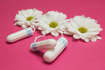 Hygienic tampons and white flowers on a pink background.