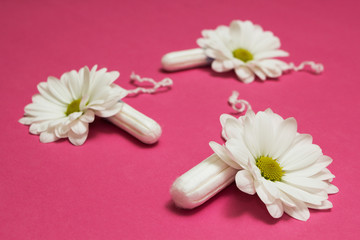 White tampons and flowers on a pink background.