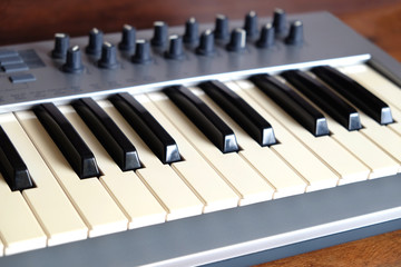 Electronic synthesizer keyboard with many control knobs in silver plastic body on wooden background side view closeup