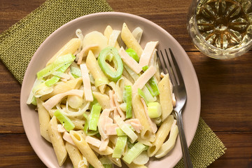 Pasta dish with ham and leek in cream sauce served on plate, photographed overhead on dark wood with natural light