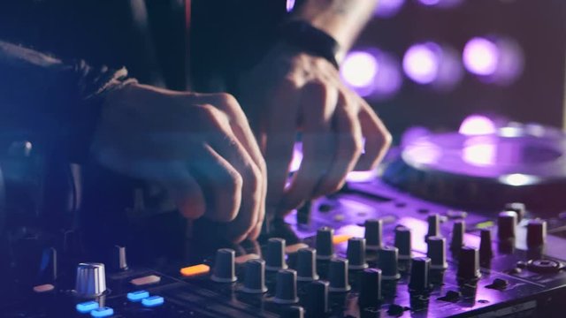 Close-up. Hands of DJ tweak various track controls on DJ mixer console at nightclub party. 4K.
