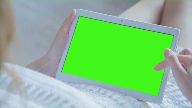 Young Woman in white dress laying on couch uses Tablet PC with pre-keyed green screen. Few types of gestures - scrolling up and down, tapping, zoom in and out. Perfect for screen compositing
