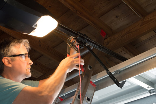 Closeup of a professional automatic garage door opener repair service technician man working on a ladder at a home residential location making adjustments and fixing it while installing it.