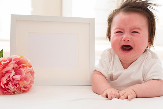 Crying baby boy with photo frame and flower