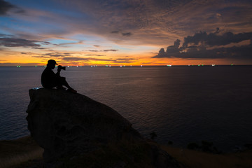 Silhouette of a man photographer sits and looks at the camera,on mountain from the view point Phuket southern of Thailand at Beautiful sunset time